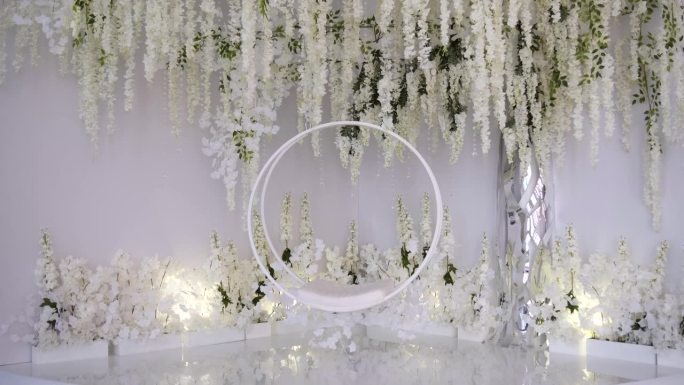 白色花丛中的圆形悬挂秋千，为新婚夫妇拍摄婚纱照。