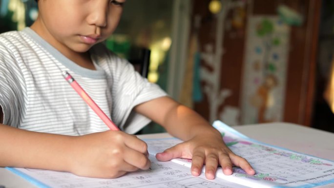 亚洲小男孩坐在课桌前写练习本的特写。小学生在家做作业，神情专注。教育理念，学习，家校。