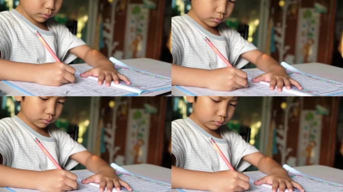 亚洲小男孩坐在课桌前写练习本的特写。小学生在家做作业，神情专注。教育理念，学习，家校。
