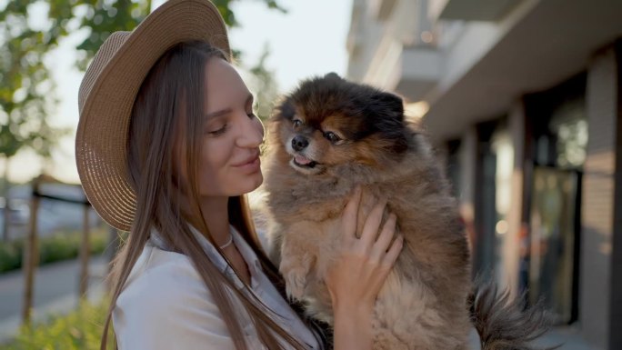 年轻女子在日落街亲吻小狗的肖像，情人女孩在散步时拥抱她的小狗。友谊的理念，潮人的生活方式，人们快乐快