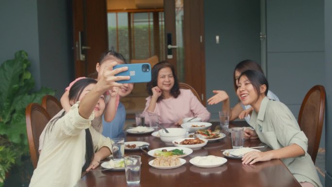 亚洲家庭用手机自拍，坐在家外后院的餐桌旁享受乐趣。多代同堂的家庭一起享受消费。