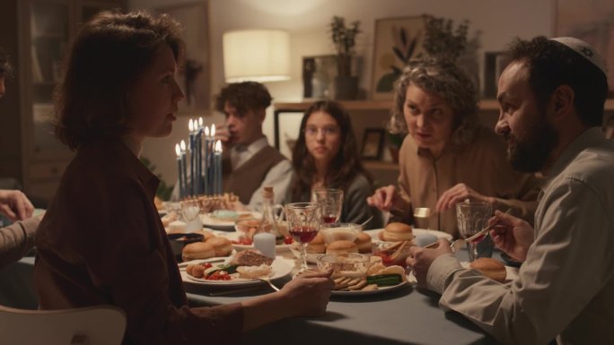 犹太男子戴着基帕帽，女子在光明节的家庭晚餐上聊天