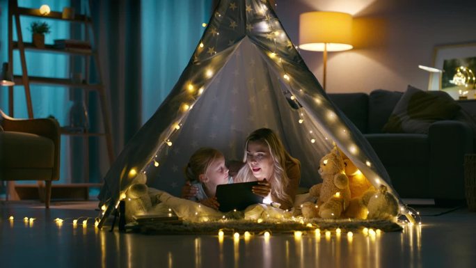 晚上，母亲和孩子在客厅的帐篷里过夜，在家里用平板电脑阅读和放松。孩子们在黑暗的房子里露营，在公寓里和