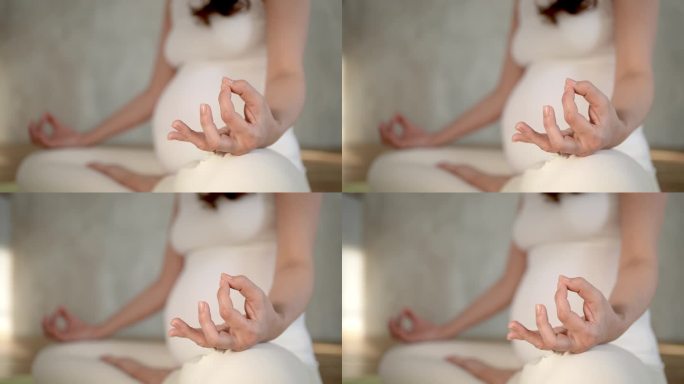 无法辨认的孕妇坐在地板上做瑜伽莲花式室内特写手。生育理念放松健康生活方式。孕妇呼吸平静练习呼吸冥想。