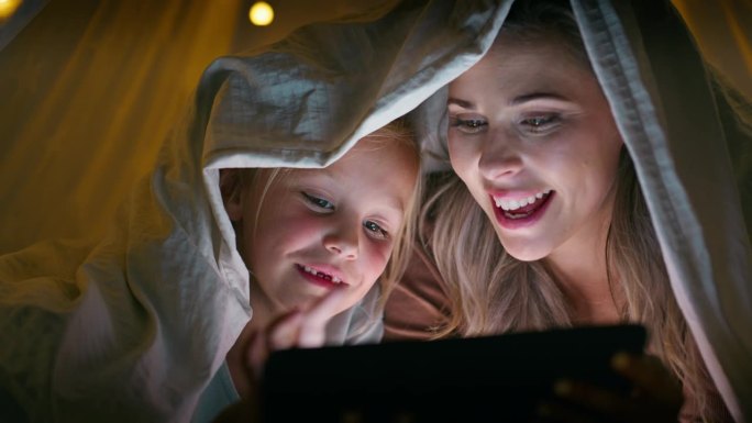 平板电脑，妈妈和孩子盖着毯子在家里过夜，晚上在灯光下看书放松。孩子们在黑暗中露营，冒险或在线讲故事，