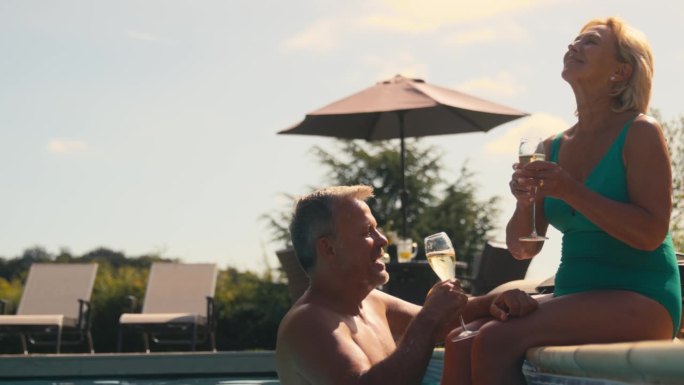 度假的老夫妇穿着泳装，在酒店游泳池旁喝香槟庆祝