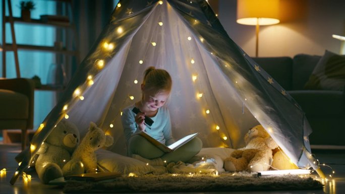 晚上，在客厅的帐篷里看书和孩子一起过夜，在家里拿着手电筒玩，放松。孩子们在黑暗的房子里露营，在公寓里
