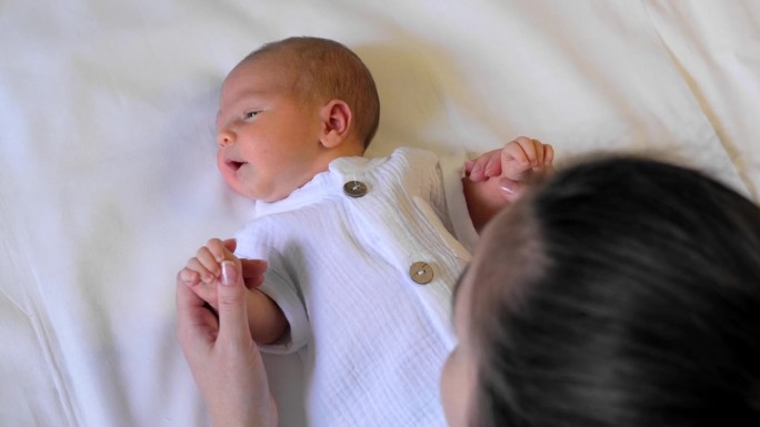 一个可爱的新生婴儿的特写肖像。一位年轻妇女双手抱着一个婴儿。母子之间的沟通，爱与关怀。