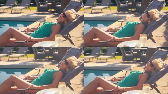 穿着泳衣的度假老妇人在酒店游泳池的躺椅上放松