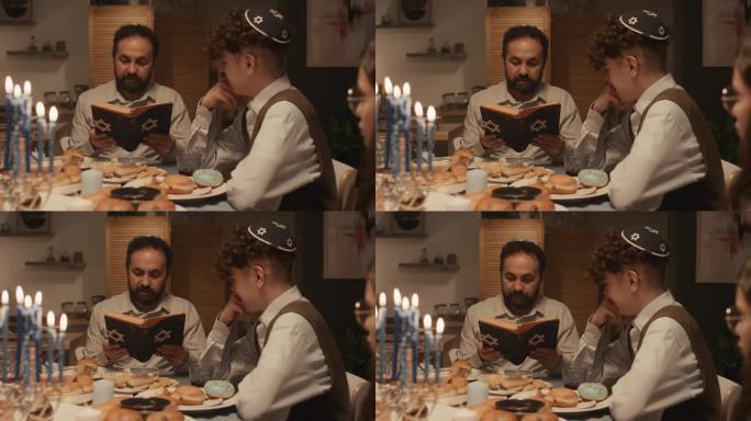 犹太父亲在基帕给十几岁的孩子们在光明节晚餐上读摩西五经