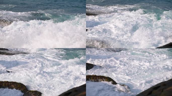 汹涌的海浪拍打着锯齿状的岩石，浪花漫射着阳光。海岸线上的动态海洋力高清捕捉。自然景观，原始力量和宁静