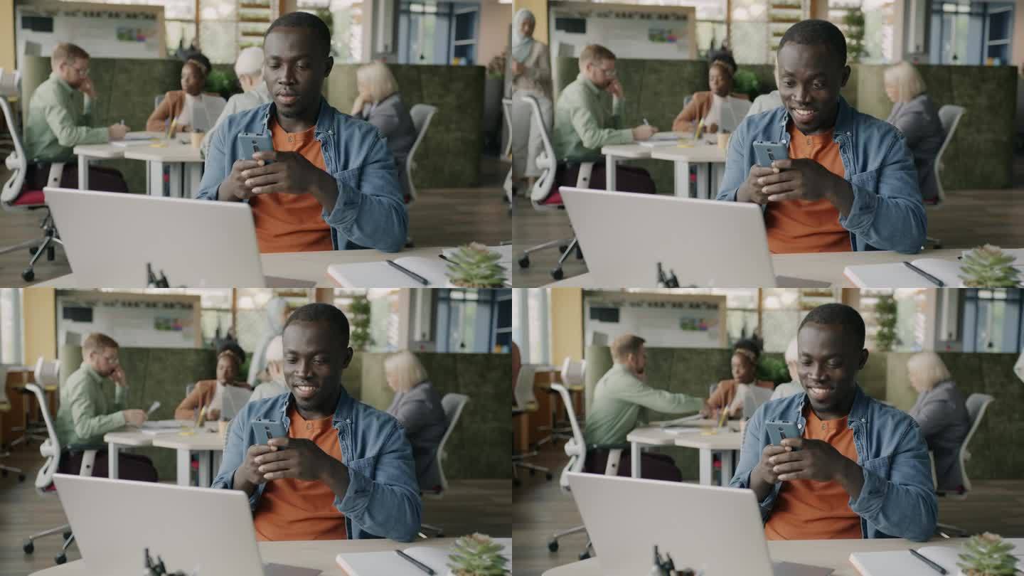 在现代办公室里，一名使用智能手机的非裔美国员工微笑着坐在办公桌前