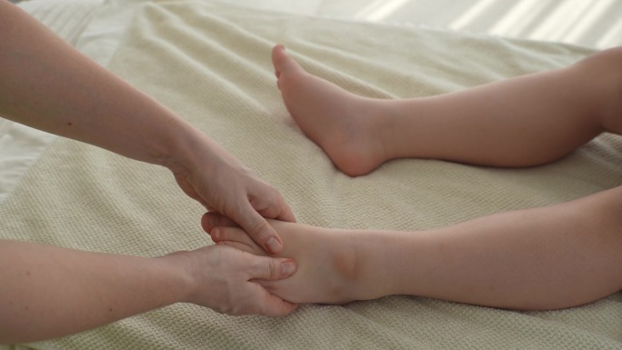 无法辨认的按摩师正在给一个五岁的小男孩按摩脚后跟，用手指按压足部穴位，预防疼痛