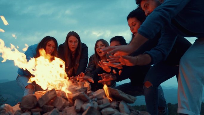 一群朋友在篝火旁的夜晚聚会上玩得很开心-友谊的生活方式概念，快乐的人在黄昏的夜晚在篝火旁取暖