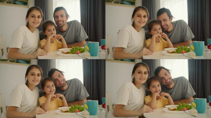 这是一个幸福快乐的家庭，一个穿灰色t恤的黑发男人，他的妻子，一个穿白色t恤的女孩，还有他们的小女儿，