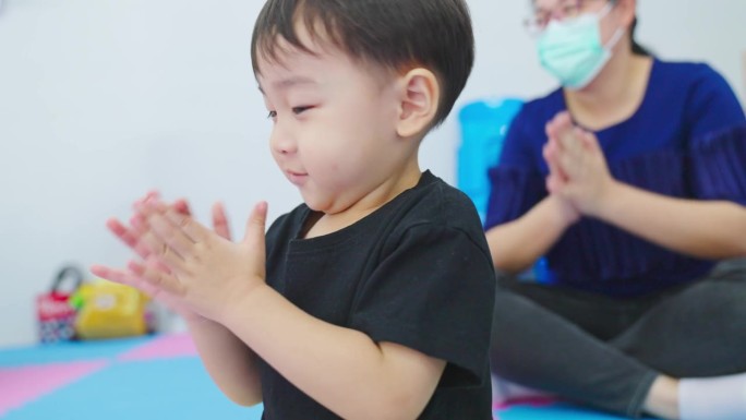 一个亚洲男孩坐下来，拍手的节奏，与他的母亲玩有节奏的活动。关于家庭纽带和课外学习的概念。