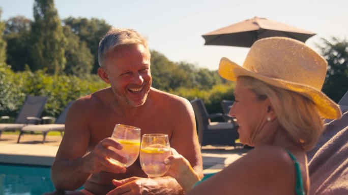 度假的老夫妇穿着泳衣在酒店游泳池边喝饮料欢呼