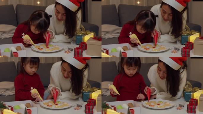 亚洲家庭圣诞快乐，新年快乐。晚上，妈妈和女儿在家里客厅的桌子上烤饼干装饰的糖霜作为圣诞礼物。