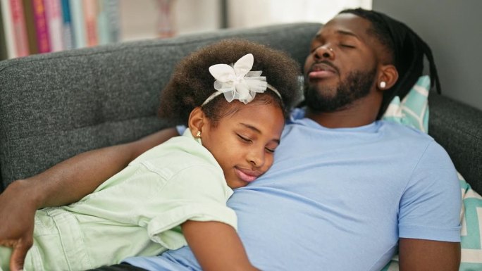 非裔美国父亲和女儿躺在家里的沙发上睡觉