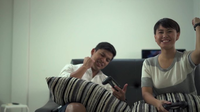 两个朋友拿着摇杆在家里的沙发上玩电子游戏。