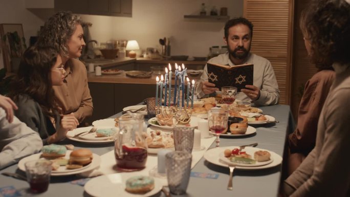 光明节最后一天，一名犹太男子在家庭晚餐上阅读《托拉经》