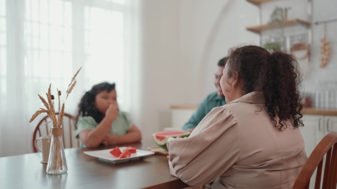 快乐的亚洲小家庭在家里享受夏日大餐，开怀大笑地吃着新鲜的西瓜。