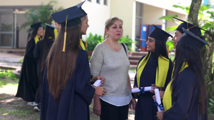 一群高中毕业生拿着毕业证书和一位妈妈交谈，他们看起来都很开心，微笑着