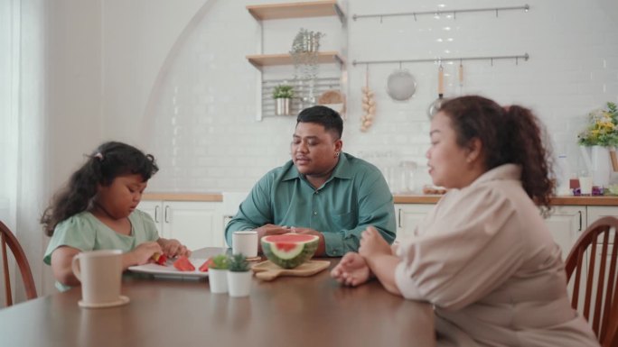 快乐的亚洲小家庭在家里享受夏日大餐，开怀大笑地吃着新鲜的西瓜。