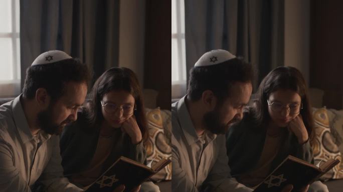戴着圆顶便帽的中年犹太男子和女儿一起读摩西五经