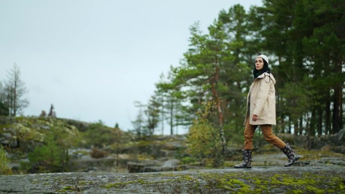 女旅行者独自行走在岩石上，背景是惊人的松树林，斯堪的纳维亚之旅