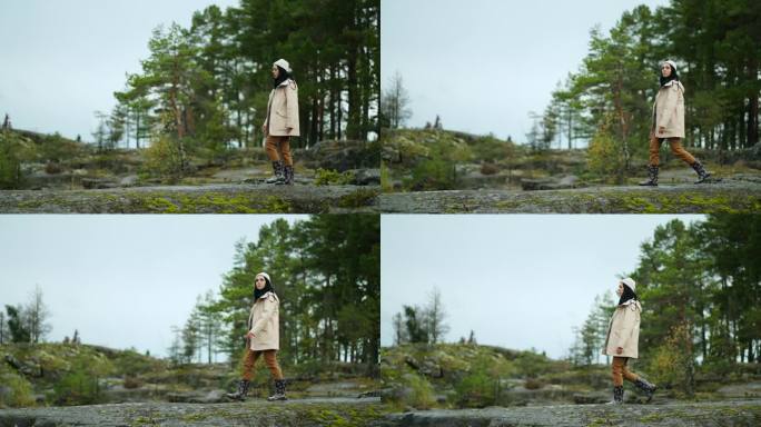 女旅行者独自行走在岩石上，背景是惊人的松树林，斯堪的纳维亚之旅