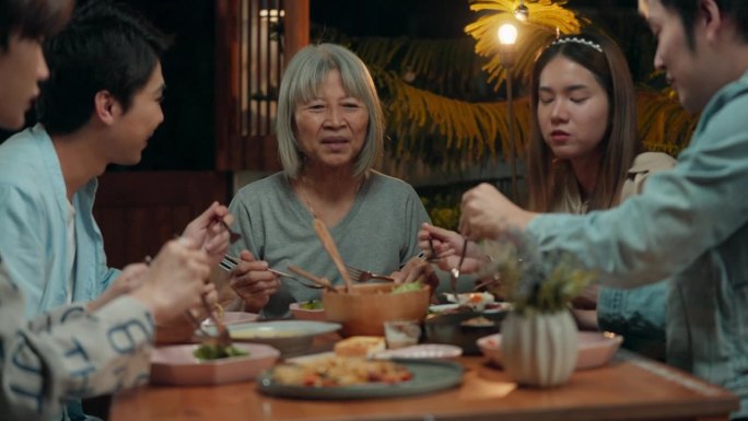 快乐的亚洲家庭围坐在餐桌旁，享受吃喝，在户外的家里一起享受晚餐，在家吃饭