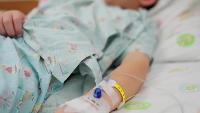 一名亚洲男孩在被诊断患有流感后在医院康复。躺在舒适的病床上，他的手连接着输注生理盐水的软管，这是他治