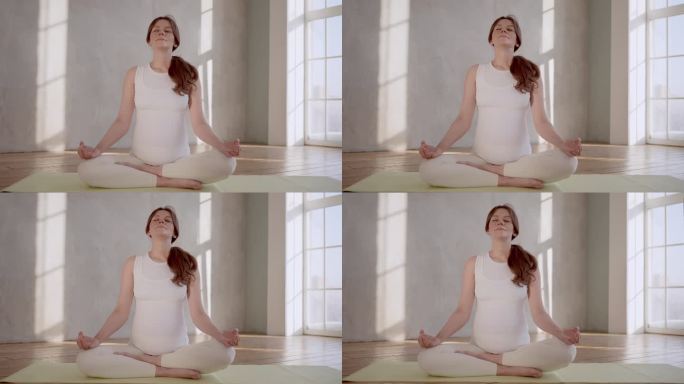 年轻的孕妇坐在地板上，在室内做瑜伽莲花式。运动锻炼孕妇理念放松健康生活方式。孕妇呼吸平静瑜伽练习呼吸