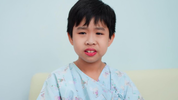 一个小男孩在医院病房里与感冒和持续的咳嗽作斗争。感到不适，用纸巾擦去鼻内的黏液。看护病人的护士在场。