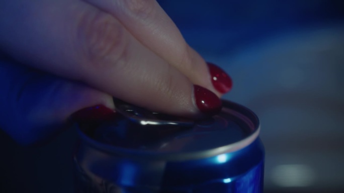 特写:红指甲的女人如何打开一个蓝色的罐装能量饮料