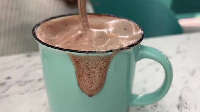 热可可饮料用金勺搅拌在一个杯子流动在一个绿色的陶瓷杯泡沫美味的巧克力饮料圣诞夜在家里休息放松的乐趣