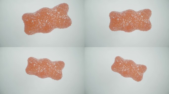 模拟小熊形状的橡皮糖落入糖中，在白色背景上旋转。
