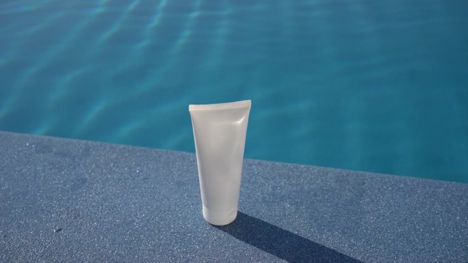 在游泳池蓝色的海水背景下，白天阳光照射下的一管奶油的白色模型。脸部和身体皮肤的润肤霜和防晒霜的概念，