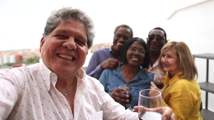 一群兴高采烈的老年人在节日庆祝大餐上自拍，对着镜头微笑。多种族的退休老人一起玩乐。