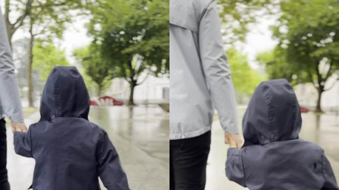 在一个阴雨的日子里，母亲和年幼的儿子手牵着手，裹着暖和的衣服，沿着林荫道和老建筑旁边的人行道散步