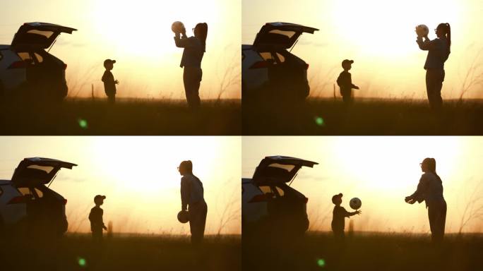 日落时分，妈妈和儿子在一辆开着后备箱的汽车旁玩球。一个幸福的家庭。夏日阳光下一家人的剪影。友好家庭的