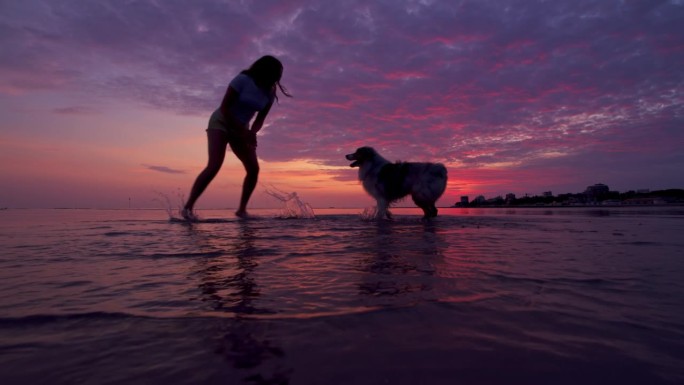 日落时分，一名年轻女子和他的狗光着脚在沙滩上奔跑