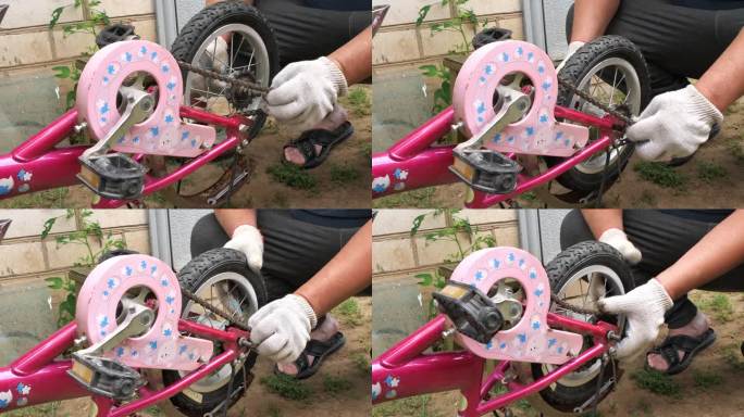 父亲修理了孩子的粉红色自行车，并更换了车轮和链条。一名戴着手套的男子正在修理一辆儿童自行车的小轮子。