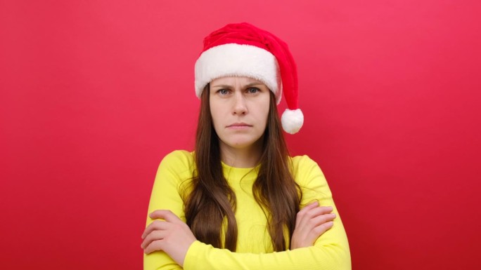 年轻女子穿着黄色毛衣，戴着圣诞老人的帽子，手里拿着食指指着时钟，在红色背景上独自摆姿势。2024年庆