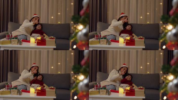 亚洲家庭圣诞快乐，新年快乐，节日庆祝。妈妈和女儿在家里装饰圣诞树。妈妈和女婴一起躺在舒适的沙发上，用