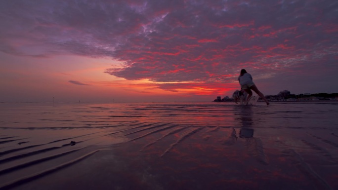 在紫色的夕阳下，一名女子和她的狗在沙滩上玩耍