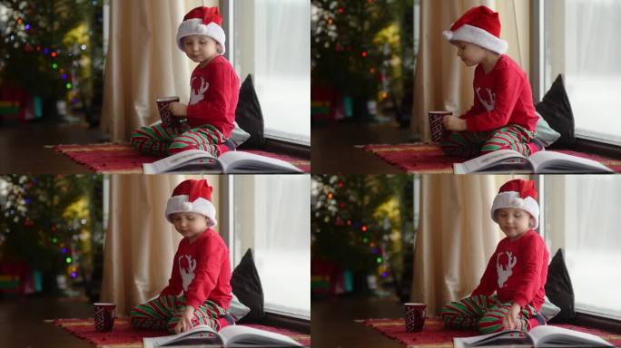温馨的圣诞节早晨:满身巧克力的可爱小男孩坐在全景窗边，看着飘落的雪花，读着一本讲节日故事的书。