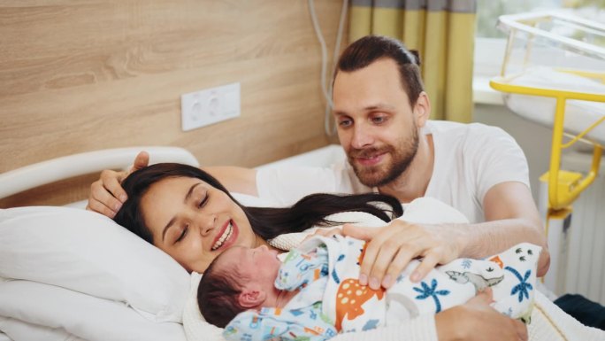 在分娩中心，刚出生的男婴被新妈妈和新爸爸抱着。初为父母的脸上洋溢着喜悦和幸福的情绪。快乐的多民族家庭