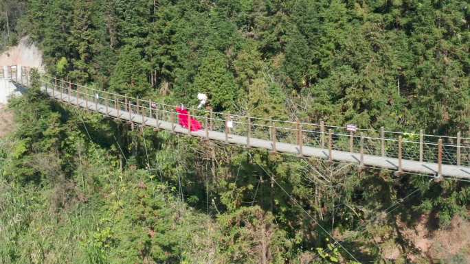 红裙女子牵着卡通气球在悬崖吊桥奔跑看风景